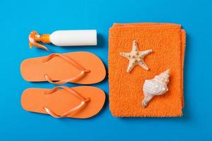 Top view of Beach flat lay accessories. sunscreen bottle with seashells, starfish, towel and flip-flop on Colored background with copy space photo