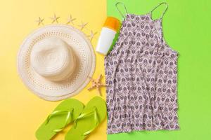 Summer accessories with t-shirt, seashells, sunscreen bottle and straw hat on yellow and green background top view flat lay photo