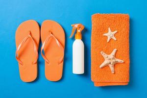 Top view of Beach flat lay accessories. sunscreen bottle with seashells, starfish, towel and flip-flop on Colored background with copy space photo