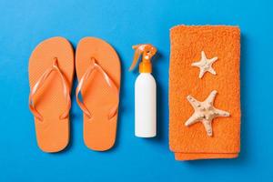 Top view of Beach flat lay accessories. sunscreen bottle with seashells, starfish, towel and flip-flop on Colored background with copy space photo