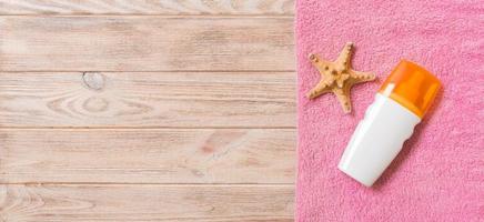 Beach flat lay accessories with copy space. Pink towel, starfish and a bottle of sunblock on wooden background. Summer holiday concept photo