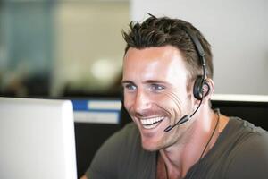 un hombre americano sonriente, sentado a su escritorio en un auriculares, Listo a recoger arriba el teléfono y ayuda clientes. trabajando en un llamada centro. generativo ai foto