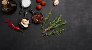 Miniature pans with spices, salt, black pepper and fragrant pepper, a sprig of rosemary on a black table. Spices for cooking photo