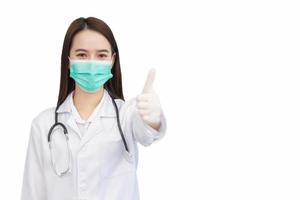 Asian professional woman doctor who wears medical coat and face mask shows thump up as good sign in health protection concept at hospital. photo