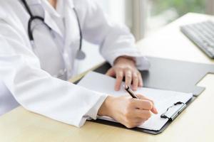 Professional female doctor is writing a report on a patient's condition in a hospital examination room. photo