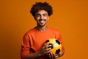 Cheerful young man holding soccer ball and looking at camera isolated over solid color background photo