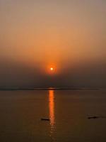 Sunset at the beach in the evening. A boat is going down the river with the sun setting behind it. photo