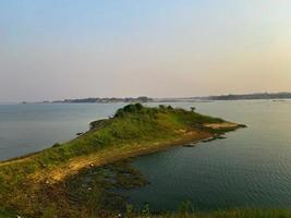 A small island in the water with the sun setting behind it. Landscape of the lake in the evening. photo