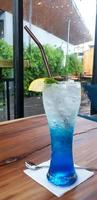 azul Hawai italiano soda cóctel con marrón tubo, limón rebanadas y verde hierba hojas en parte superior de vaso en de madera mesa con dentro café tienda antecedentes. refresco Bebiendo y vida estilo comiendo foto