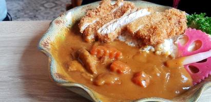 Close up hot spicy Japanese curry with fried pork and rice in plate on the wooden table. Delicious food and Special meal concept. photo