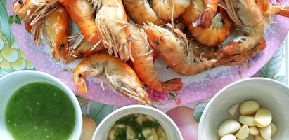 Many Grilled giant river shrimp or prawn in white plate with spicy sauce and fresh garlic for serving customer or sale at seafood restaurant. Group of animal, Food, Barbeque party and Lunch tim photo