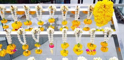 Many garland flower hanging on white stainless steel hanger for worship the Buddha at Thai temple. Religion, Culture and Respect or Faith concept photo