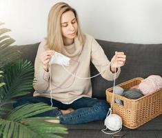 Young woman knitting warm scarf indoors photo