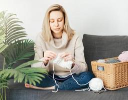 Young woman knitting warm scarf indoors photo