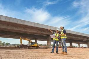 Asian architect and mature supervisors meeting at construction site Multiethnic workers and engineers discussing plans Two construction workers working together while visiting expressway construction photo