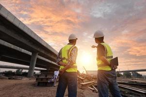 asiático arquitecto y maduro supervisores reunión a construcción sitio multiétnico trabajadores y ingenieros que se discute planes dos construcción trabajadores trabajando juntos mientras visitando Autopista construcción foto