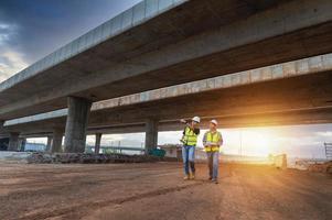 asiático arquitecto y maduro supervisores reunión a construcción sitio multiétnico trabajadores y ingenieros que se discute planes dos construcción trabajadores trabajando juntos mientras visitando Autopista construcción foto