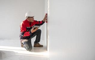 un construcción trabajador o arquitecto vistiendo un difícil sombrero es comprobación el pared con un nivel indicador. foto