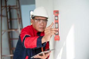 un construcción trabajador o arquitecto vistiendo un difícil sombrero es comprobación el pared con un nivel indicador. foto