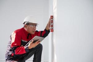 un construcción trabajador o arquitecto vistiendo un difícil sombrero es comprobación el pared con un nivel indicador. foto