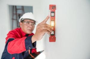 un construcción trabajador o arquitecto vistiendo un difícil sombrero es comprobación el pared con un nivel indicador. foto