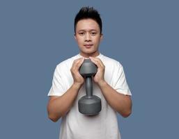 Young man is exercising using dumbbells isolated on plain background photo
