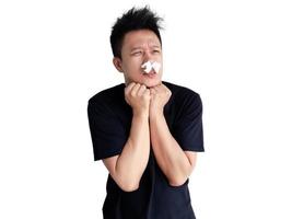 Young man with shivering expression with tissue on nose and clasping hands photo