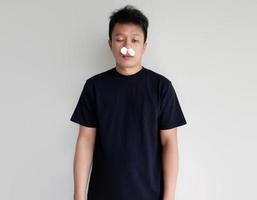 joven hombre con plano y cansado facial expresión con pañuelo de papel en fosa nasal foto