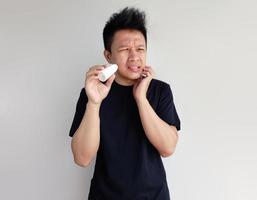 Young man is rubbing toothache medicine on the cheek isolated on plain background photo