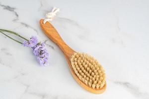 Dry massage brush with natural bristle on marble backgorund, ecolodical cosmetics, home care spa procedures. photo