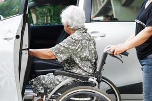 cuidador ayuda a una anciana asiática con discapacidad a entrar en su automóvil, concepto médico. foto