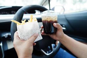 Asian woman driver hold and eat french fries in car, dangerous and risk an accident. photo