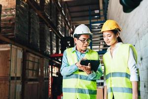 Working at warehouse. asian woman warehouse worker and Manager Shows Digital Tablet Information to further placement in storage department. In Background Stock of Parcels with Products photo