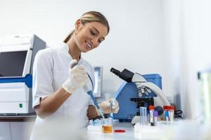 Woman biologist using micro pipette with test tube and beaker for experiment in science laboratory. Biochemistry specialist working with lab equipment and glassware for development. photo