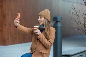 mujer sentado en el banco en el ciudad parque ,Bebiendo café y utilizando móvil teléfono foto