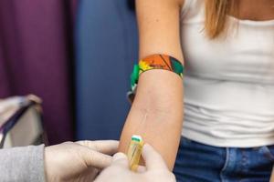 preparación para sangre prueba con bonito joven mujer por hembra médico médico uniforme en el mesa en blanco brillante habitación. enfermero perfora el del paciente brazo vena con aguja blanco tubo foto