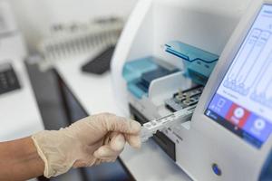 Female laboratory assistant making analysis with test tubes and analyzer machines sitting at the modern laboratory, lab tech loading samples into a chemistry analyzer photo