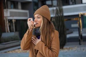 Side view portrait of an asthmatic woman using a inhaler outdoors in the street. Young woman standing at street, she blocked asthma atack photo