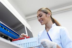 Portrait of a young female laboratory assistant making analysis with test tubes and analyzer machines sitting at the modern laboratory photo