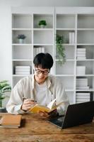 Handsome and talented young Asian man student working on his project assignment, using laptop and tablet to search an online informations. photo