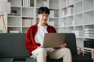 Young attractive Asian man smiling thinking planning writing in notebook, tablet and laptop working from home  at home office photo