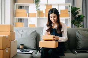 Young asian business owner woman prepare parcel box and standing check online orders for deliver to customer on tablet, laptop Shopping Online concept. photo