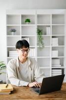 Handsome and talented young Asian man student working on his project assignment, using laptop and tablet to search an online informations. photo