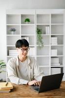 Handsome and talented young Asian man student working on his project assignment, using laptop and tablet to search an online informations. photo