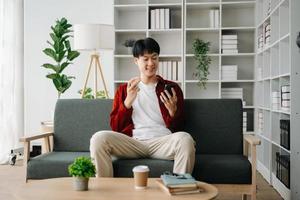 Young attractive Asian man smiling thinking planning writing in notebook, tablet and laptop working from home  at home office photo