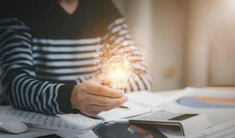Creativity and innovation are keys success concept, businessman hand holding light bulb with using calculator to calculate and money stack. idea saving energy and accounting finance in office concept photo