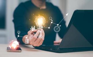 Businessman holding a bright light bulb, creativity with light bulbs and energy power, hand of a man with a light bulb and line light icon and using a notebook computer, technology innovation idea photo