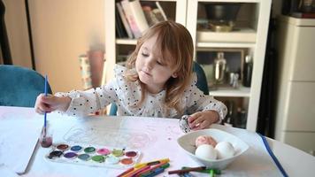 klein Mädchen Sitzung beim Tabelle Gemälde Ostern Eier mit Wasser Farben 4k video