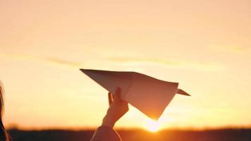 Woman launches paper airplane against sunset background. Concept of wanting to go on vacation or travel. Slow motion video