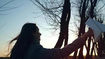 Woman launches paper airplane against sunset background. Concept of wanting to go on vacation or travel. Slow motion video